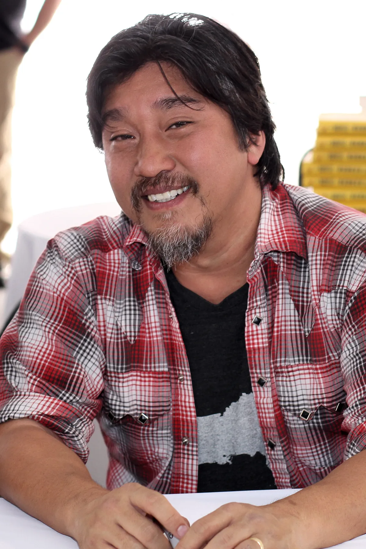 Chef Edward Lee in a plaid shirt smiling at a book-signing table